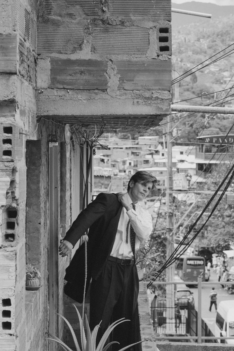 Monochrome fashion editorial featuring a male model putting on a suit jacket outdoors in an urban setting.