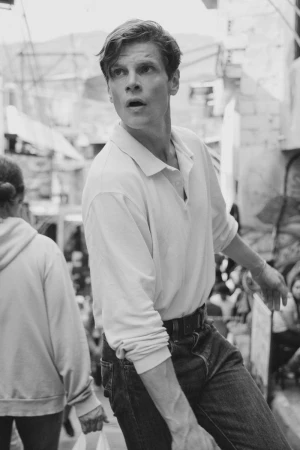 Black and white editorial portrait of a man in a white polo shirt and dark jeans looking upward outdoors