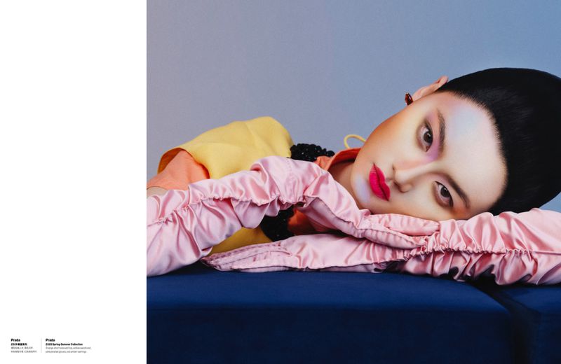Model He Cong wearing pink satin gloves and layered yellow and orange top resting on a dark blue surface for W Magazine China