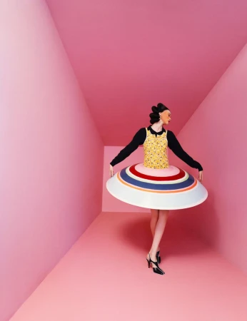 Model He Cong in a sculptural striped circular dress standing inside a pink room for W Magazine China photographed by Zhong Lin.