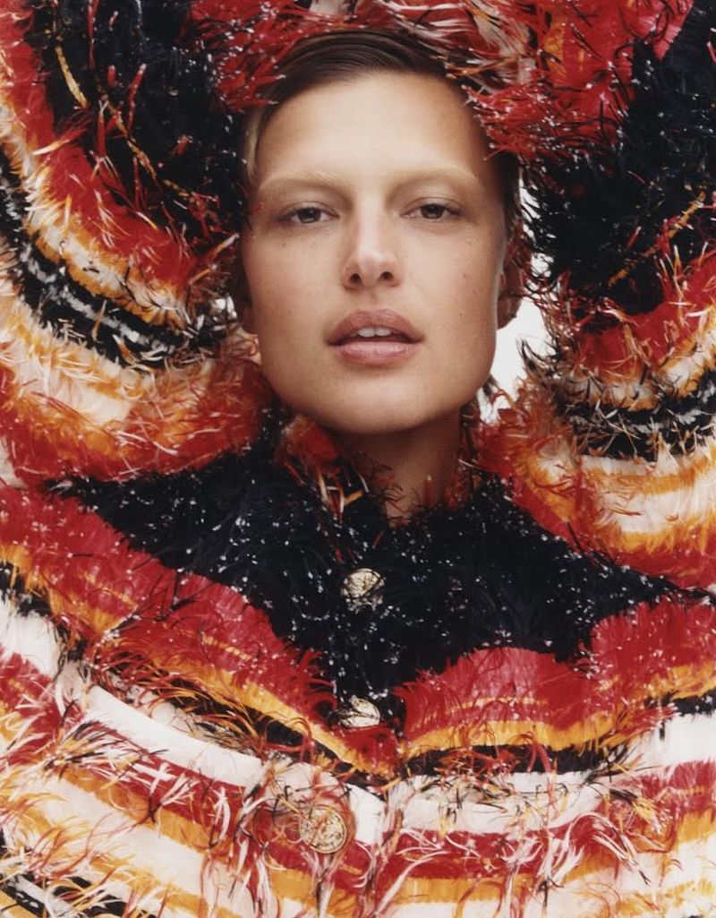 Model wearing a textured red, black, and white fringed jacket with arms raised framing her face