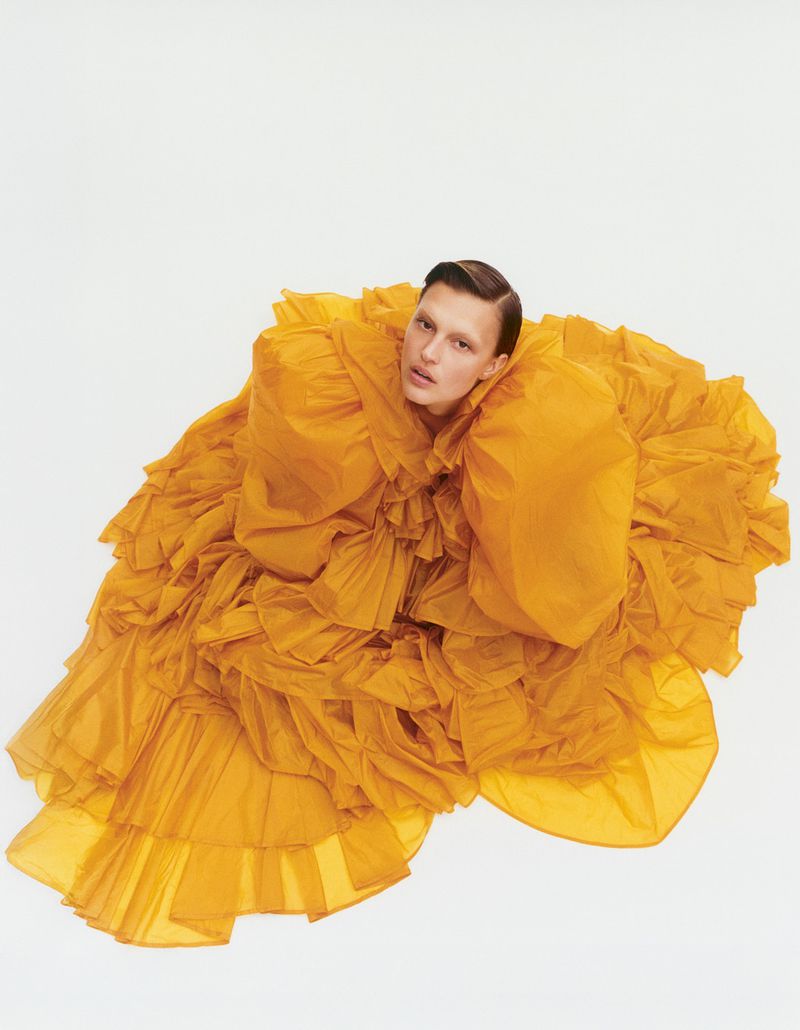 Fashion photo of a person in a large, ruffled yellow gown against a white backdrop, creating a striking and artistic visual statement.