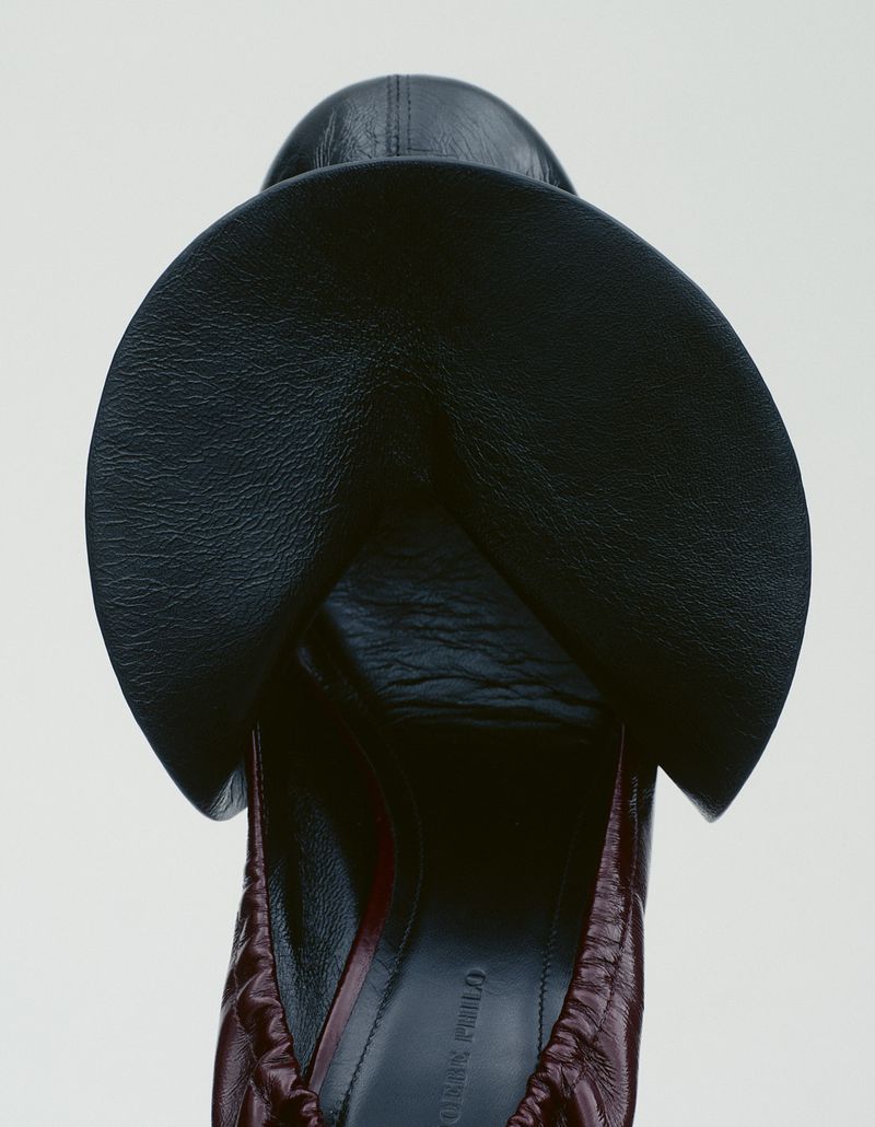 Close-up overhead shot of a black leather shoe with circular overlapping flaps against a pale background