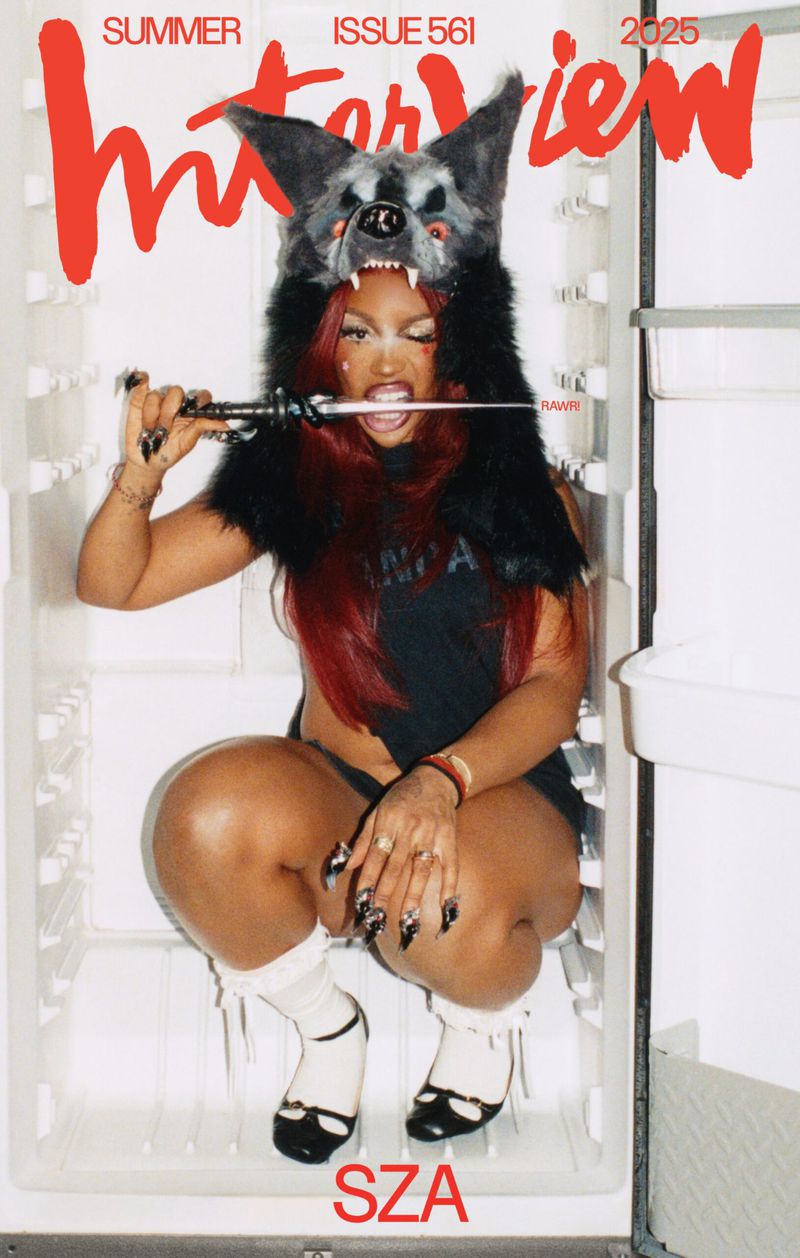 Interview magazine cover featuring a young woman in a fur hat and dark clothing crouching inside an open refrigerator.