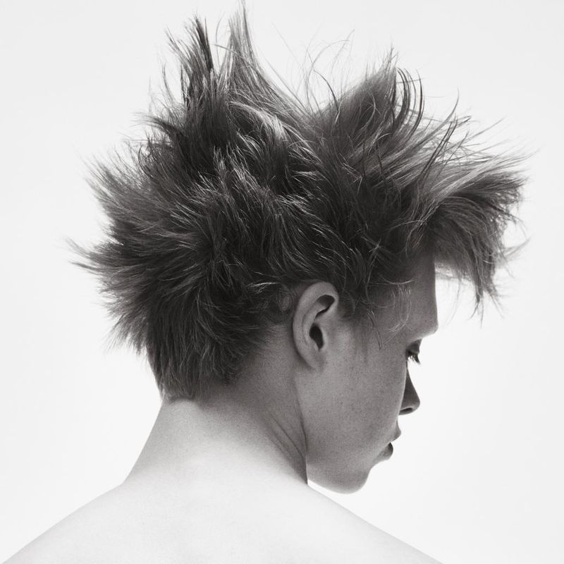 Monochrome portrait of a person with spiky dark hair against a bright white background, emphasizing the hairstyle and clean, simple aesthetic.