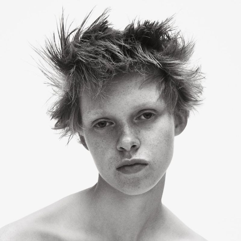 Close-up portrait of a model with short textured hair and serious expression against a bright white background