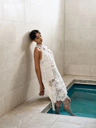 Model in white lace dress leaning against stone wall next to indoor pool for Harper's Bazaar Ecuador editorial