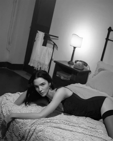 Model lying on a lace-spread bed in a bedroom for Dolce and Gabbana DNA Spring 2026 campaign.
