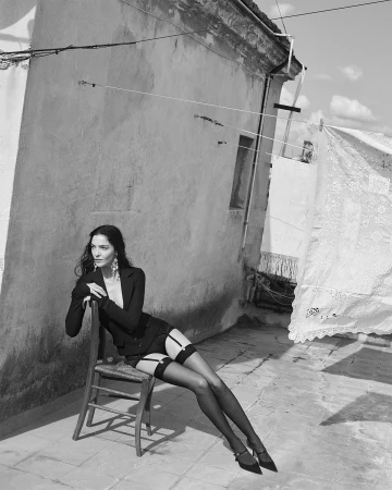 Model seated on a wooden chair on a rooftop with laundry hanging on a clothesline in black and white