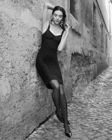Model in a black dress leaning against a rustic stone wall on a cobblestone alley in Rome for Dolce & Gabbana