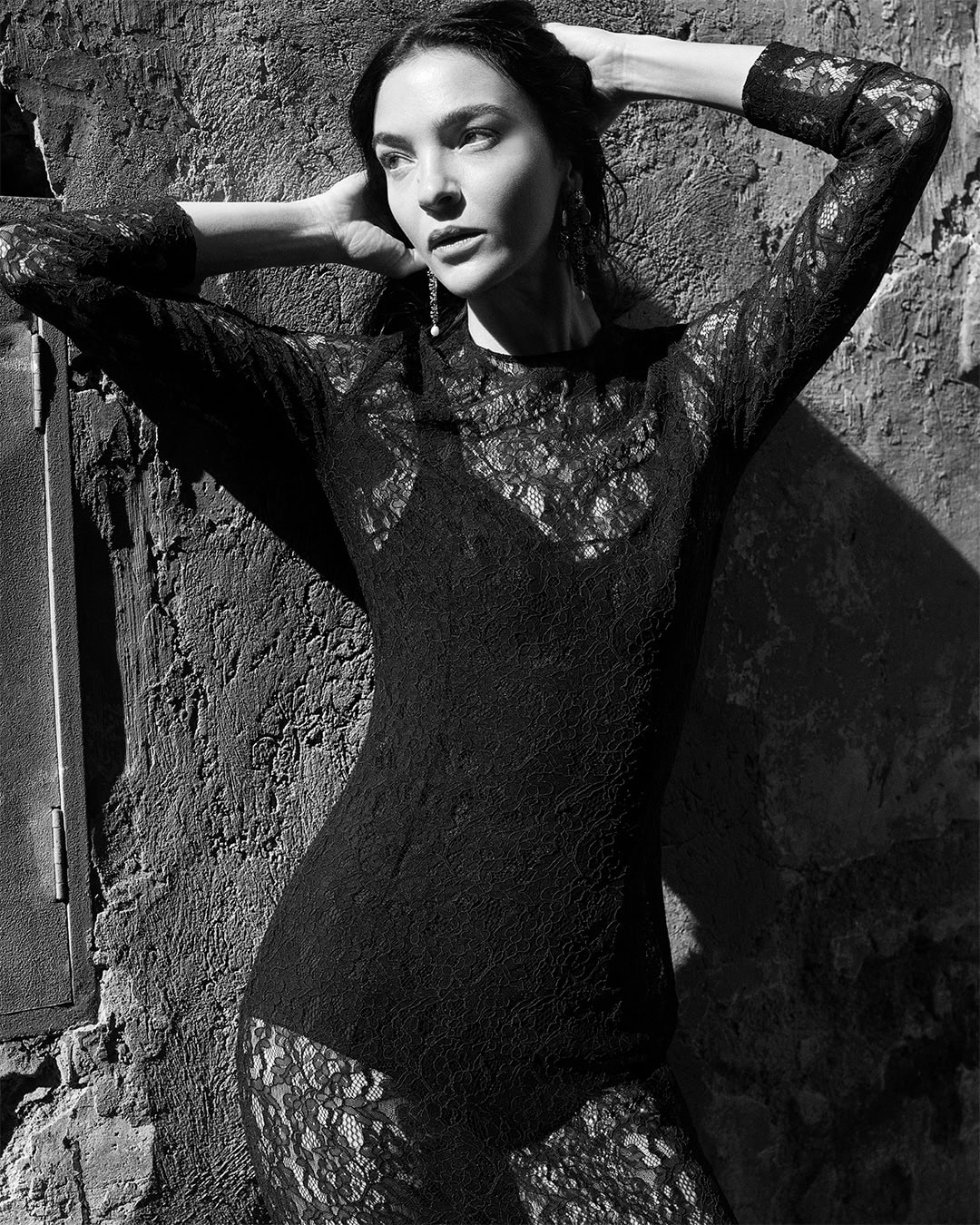 Model Mariacarla Boscono in a black lace dress posing against a textured wall for Dolce & Gabbana DNA Spring 2026 campaign.