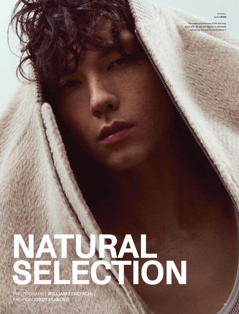 Close-up portrait of a male model wearing a textured cream hooded zip jacket against a plain sky background