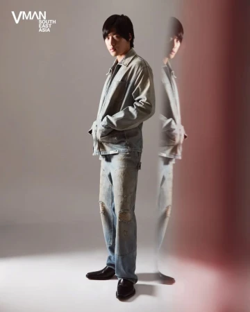 Full-length fashion portrait of a man in a denim jacket and distressed jeans against a light grey studio background.