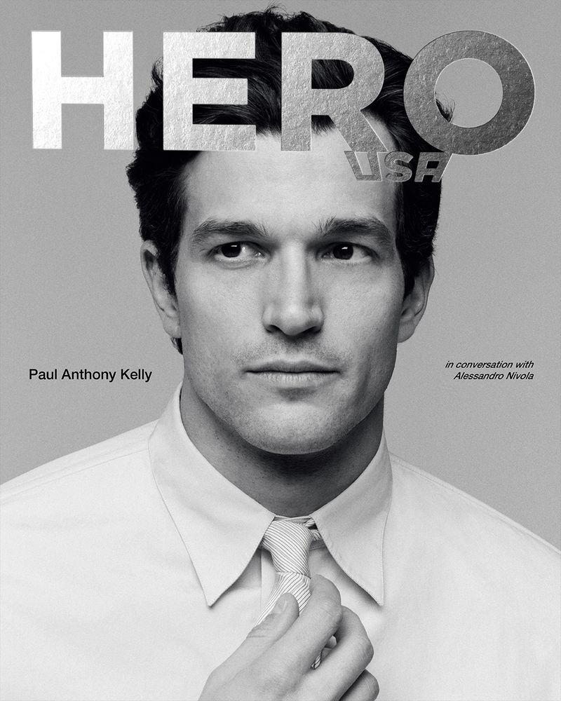 Black and white portrait of Paul Anthony Kelly on Hero USA magazine cover, adjusting tie, clean style, fashion, studio shot.