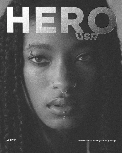 Close-up monochrome portrait of Willow Smith with braided hair and facial piercings against a plain background