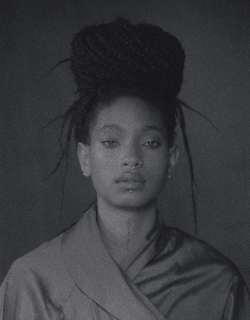 Close-up portrait of a young adult female with braided hair, wearing a satin robe against a dark gray background in black and white.