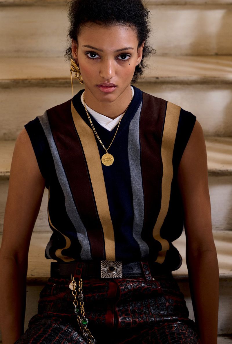 Model wearing a striped V-neck sweater and patterned trousers seated on stone steps for HERO USA