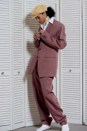 Model wearing a mauve suit and beige flat cap standing against white louvered folding doors