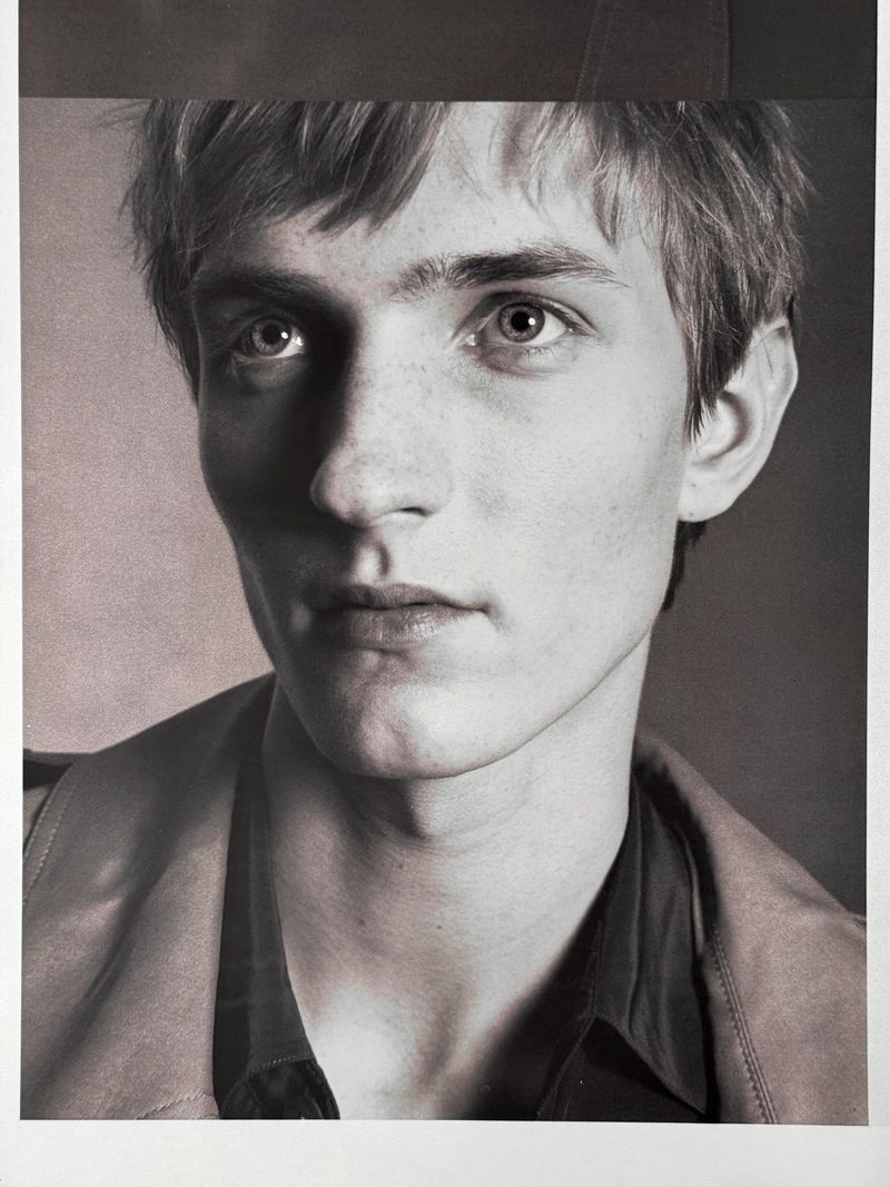 Close-up portrait of a young male model with short hair against a dark studio background for HERO USA.