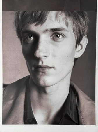 Close-up portrait of a young male model with short hair against a dark studio background for HERO USA.