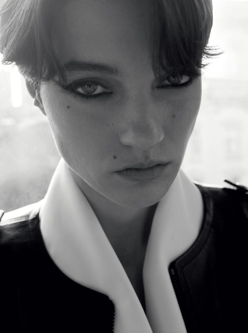 Close-up monochrome portrait of a model with dark eyeliner wearing a high-collared jacket.