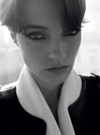 Close-up monochrome portrait of a model with dark eyeliner wearing a high-collared jacket.