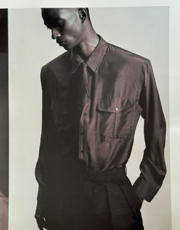 Black man wearing a long-sleeved button-down shirt and tie against a plain light studio background