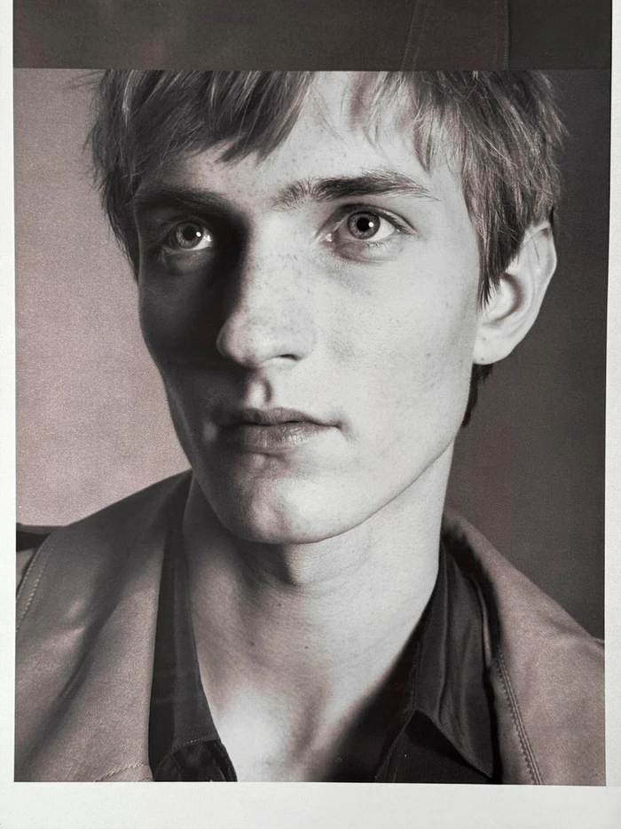 Close-up portrait of a young male model with short hair against a dark studio background for HERO USA.