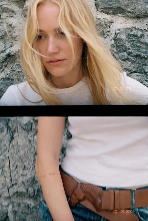Maika Monroe wearing a white t-shirt and brown belt against a stone wall for HERO USA, photographed by Dana Boulos.
