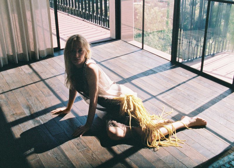 Maika Monroe reclining on wooden floorboards in a sunlit room with large windows for HERO USA photographed by Dana Boulos.