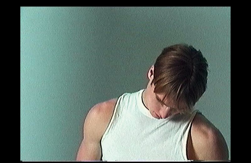 Model Henry Rank wearing a white tank top against a plain textured green background.