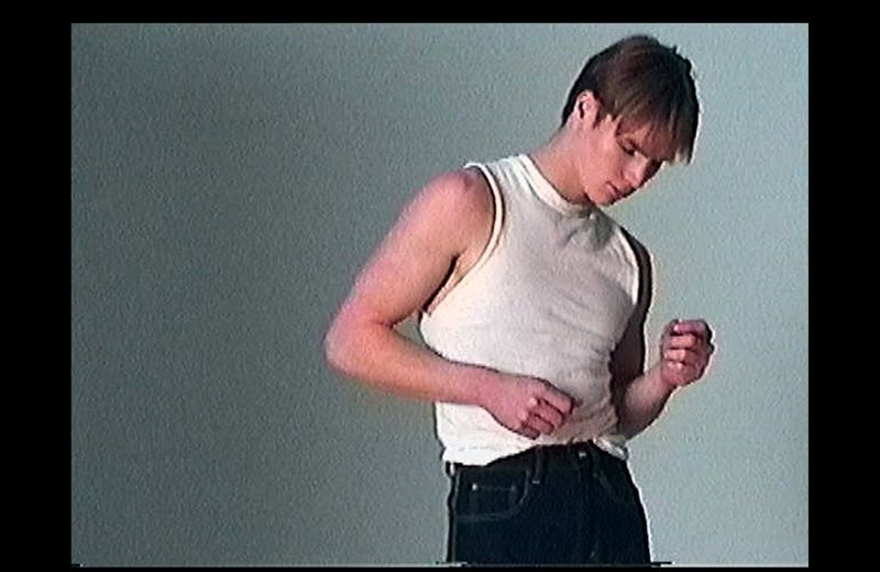 Model Henry Rank in a white tank top and dark jeans against a grey seamless background photographed by Fabien Kruszelnicki.