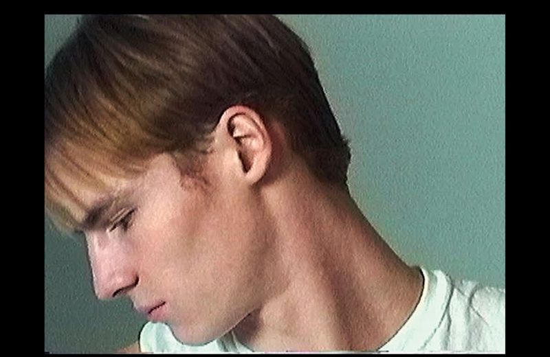 Close-up profile portrait of male model Henry Rank wearing a white t-shirt against a plain green background.