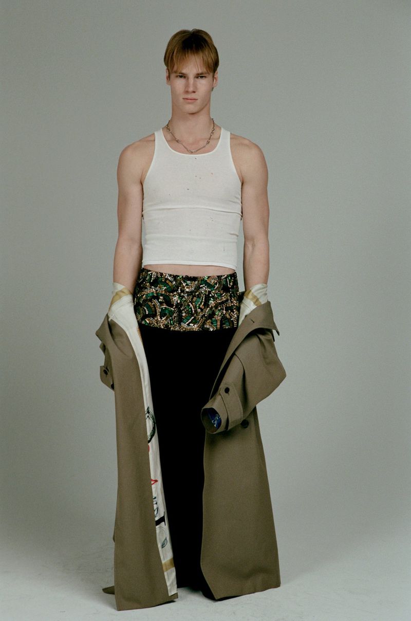 Model Henry Rank wearing a white tank top and khaki coat for HERO USA photographed by Fabien Kruszelnicki.