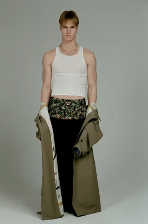 Model Henry Rank wearing a white tank top and khaki coat for HERO USA photographed by Fabien Kruszelnicki.