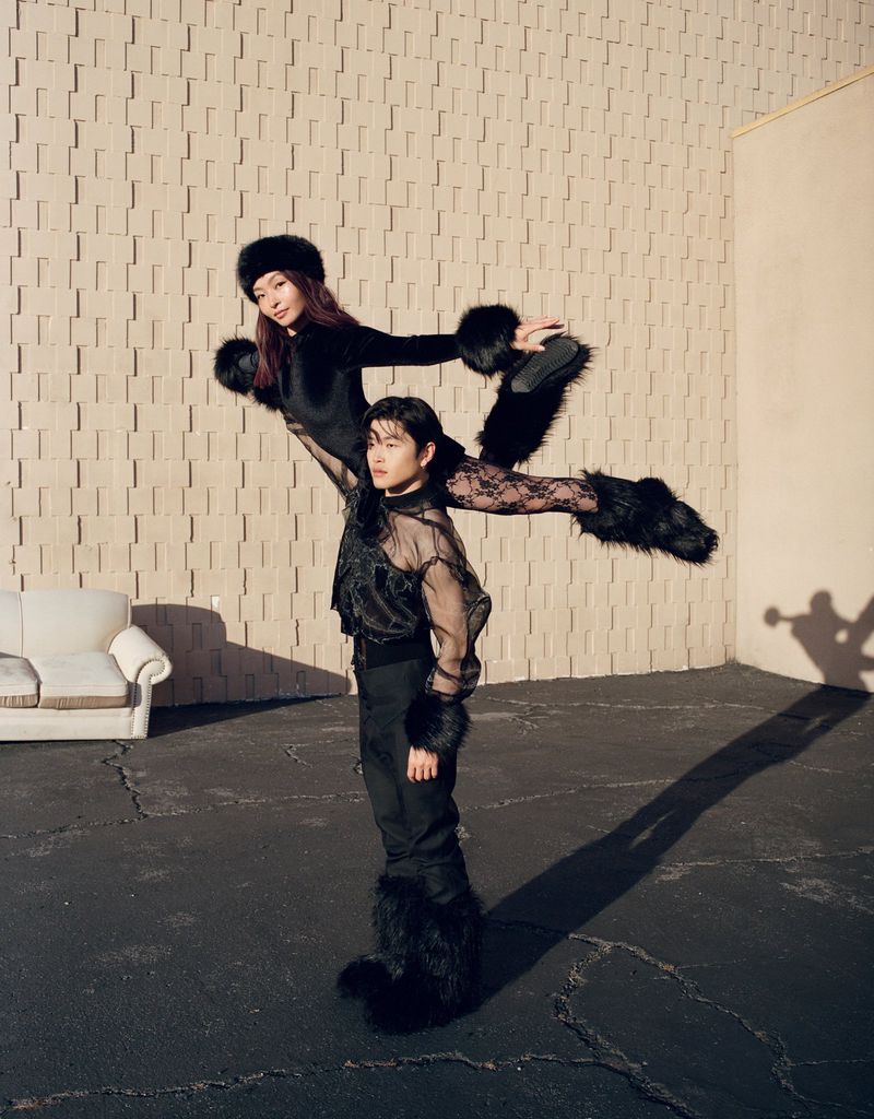 Alex and Maia Shibutani in black outfits posing outdoors against a textured concrete block wall with an outdoor sofa