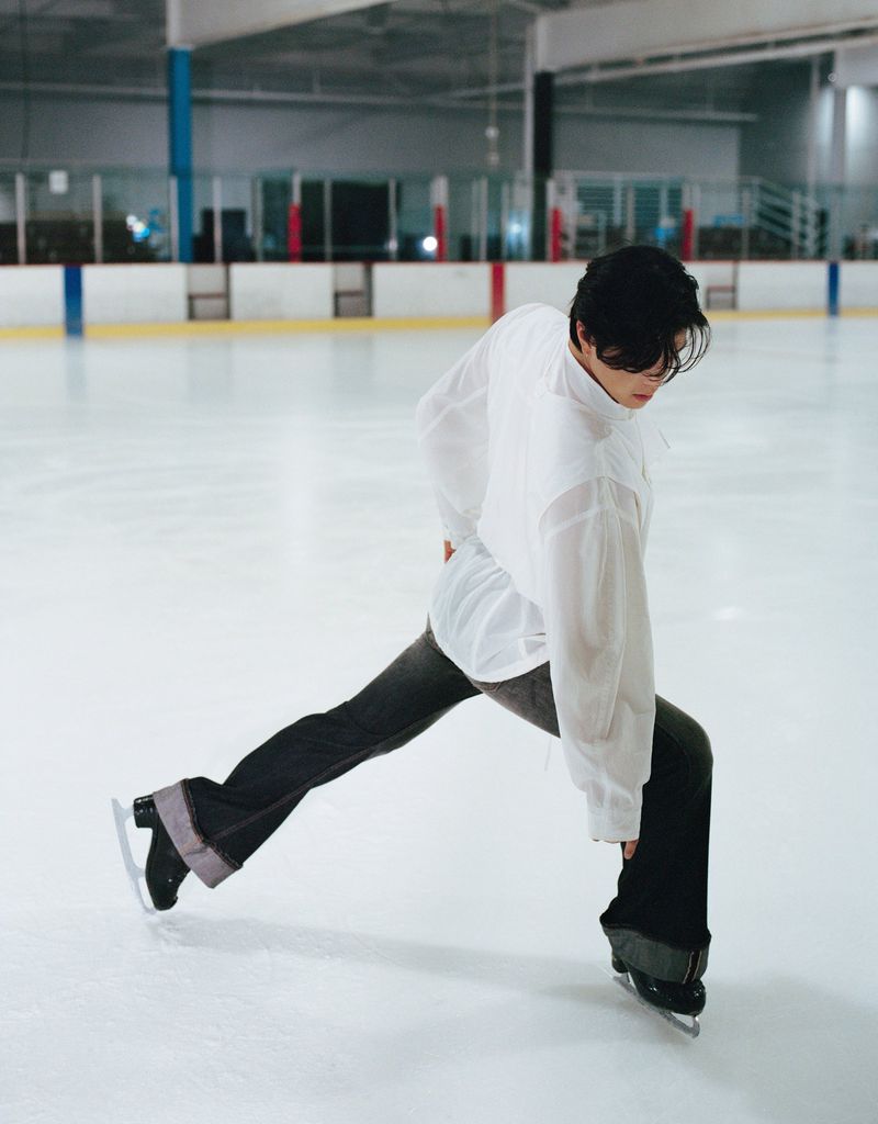 Figure skater in a white shirt and dark trousers performing on an indoor ice rink for HERO USA.
