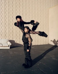 Alex and Maia Shibutani in black outfits posing outdoors against a textured concrete block wall with an outdoor sofa