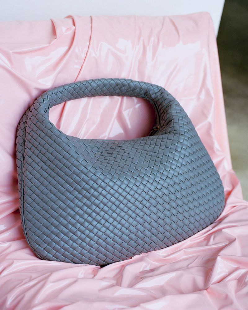Grey woven leather handbag resting on a glossy pink draped backdrop for HERO USA Things That Choose You