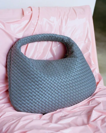 Grey woven leather handbag resting on a glossy pink draped backdrop for HERO USA Things That Choose You