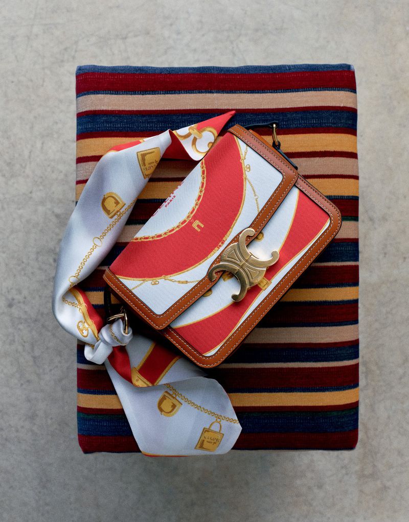 Structured top-down studio shot of a patterned leather handbag resting on a colourful striped textile surface.
