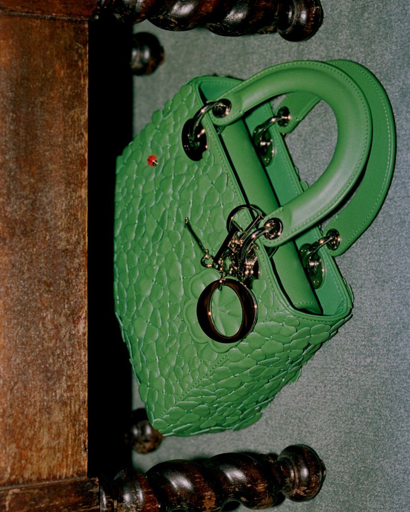 Close-up studio shot of a bright green leather Lady Dior handbag with silver hardware on a wooden surface and dark grey wall.