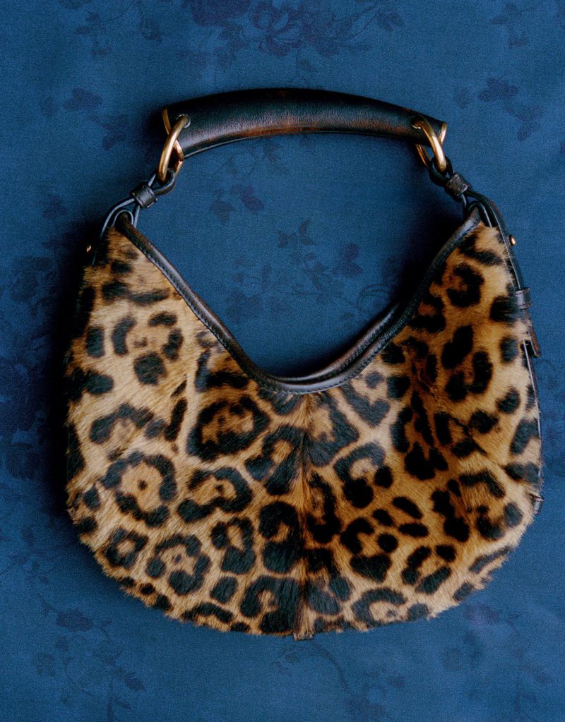 Leopard print faux fur handbag with black leather trim and top handle against a textured blue background.