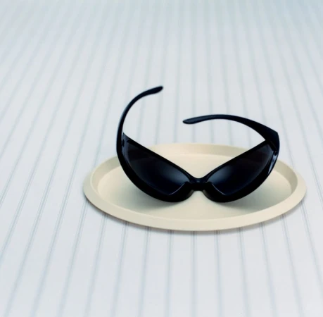Black sunglasses resting inside a pale beige small circular tray on a striped white surface.