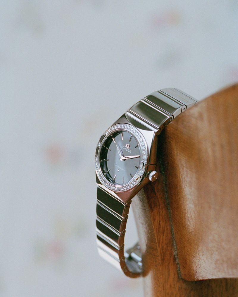 Silver luxury wristwatch with a dark dial and diamond bezel resting against a polished wooden surface
