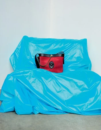 Red handbag with black leather trim resting on a bright blue crinkled plastic-covered furniture piece against a white wall