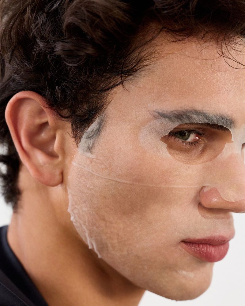Close-up profile of a man wearing a white facial sheet mask against a clean neutral background for GQ China.