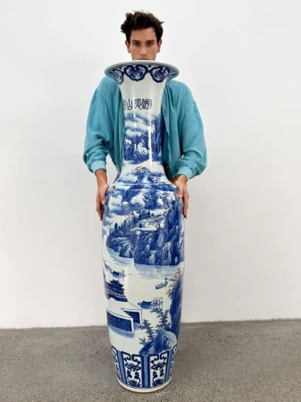 Model standing behind a large blue and white porcelain vase against a plain white studio background for GQ China