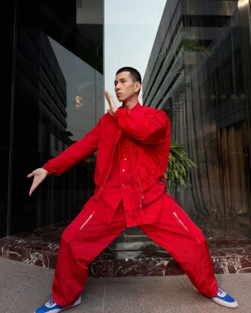 Man in bright red jacket and matching pants striking a martial arts pose outside a modern building.