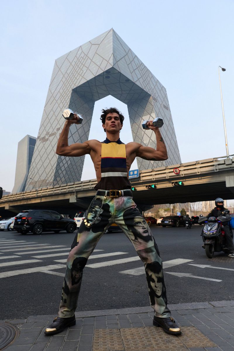 A man in patterned trousers holding dumbbells poses on a city street before a striking modern architectural structure for GQ China.